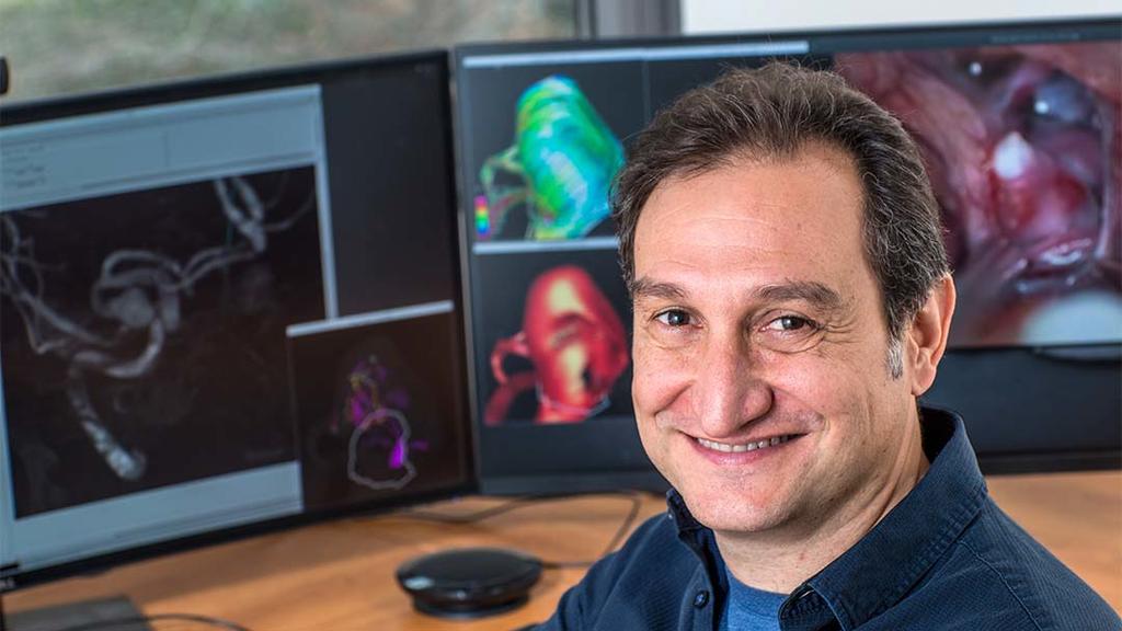 Juan Cebral sits in front of computers with brain scans on the screens