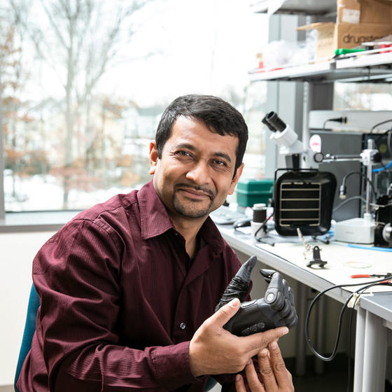 Sikdar poses in a lab holding a smart prosthetic hand. 